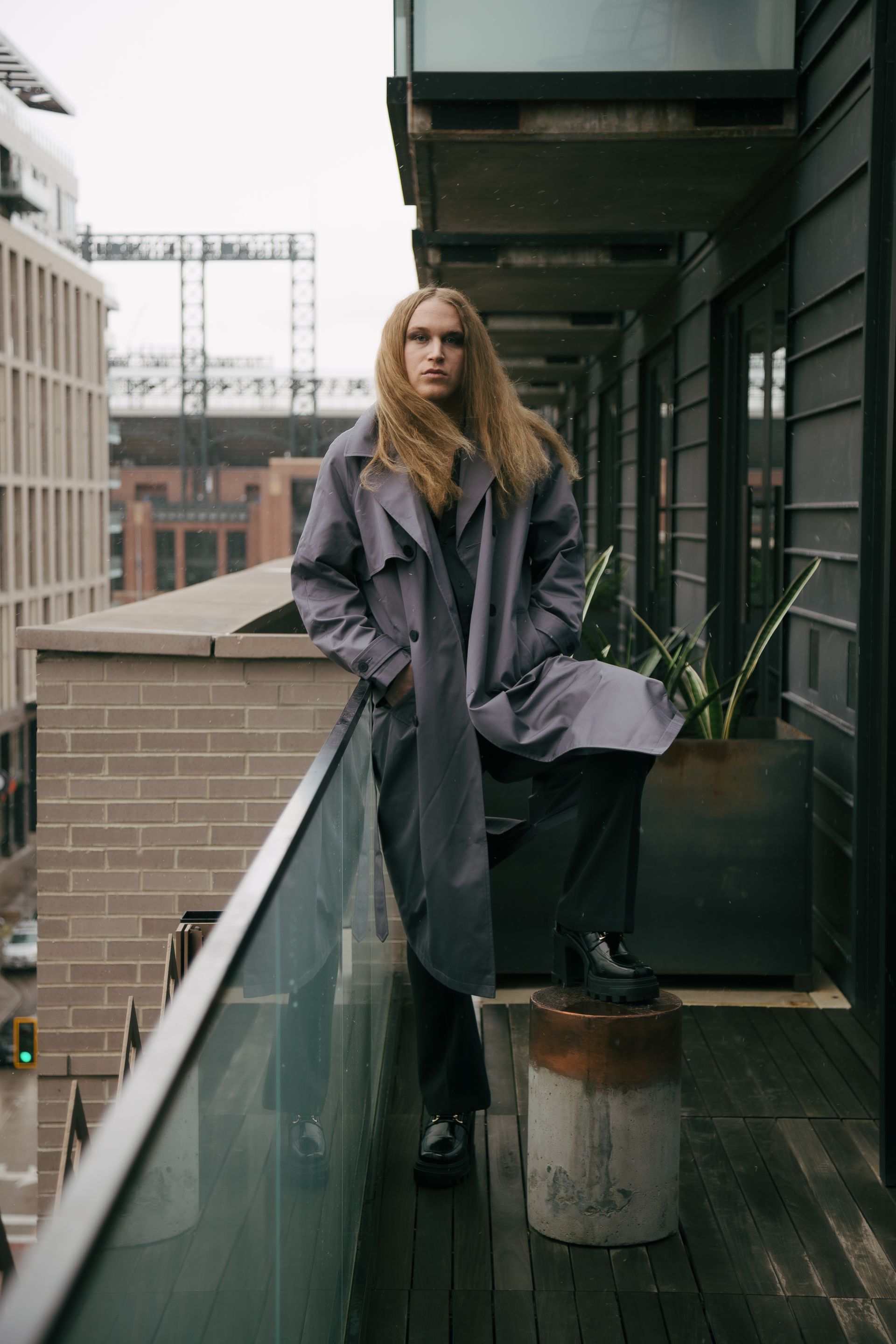 Scotty in a trench coat is standing on a balcony for a fashion photo shoot.