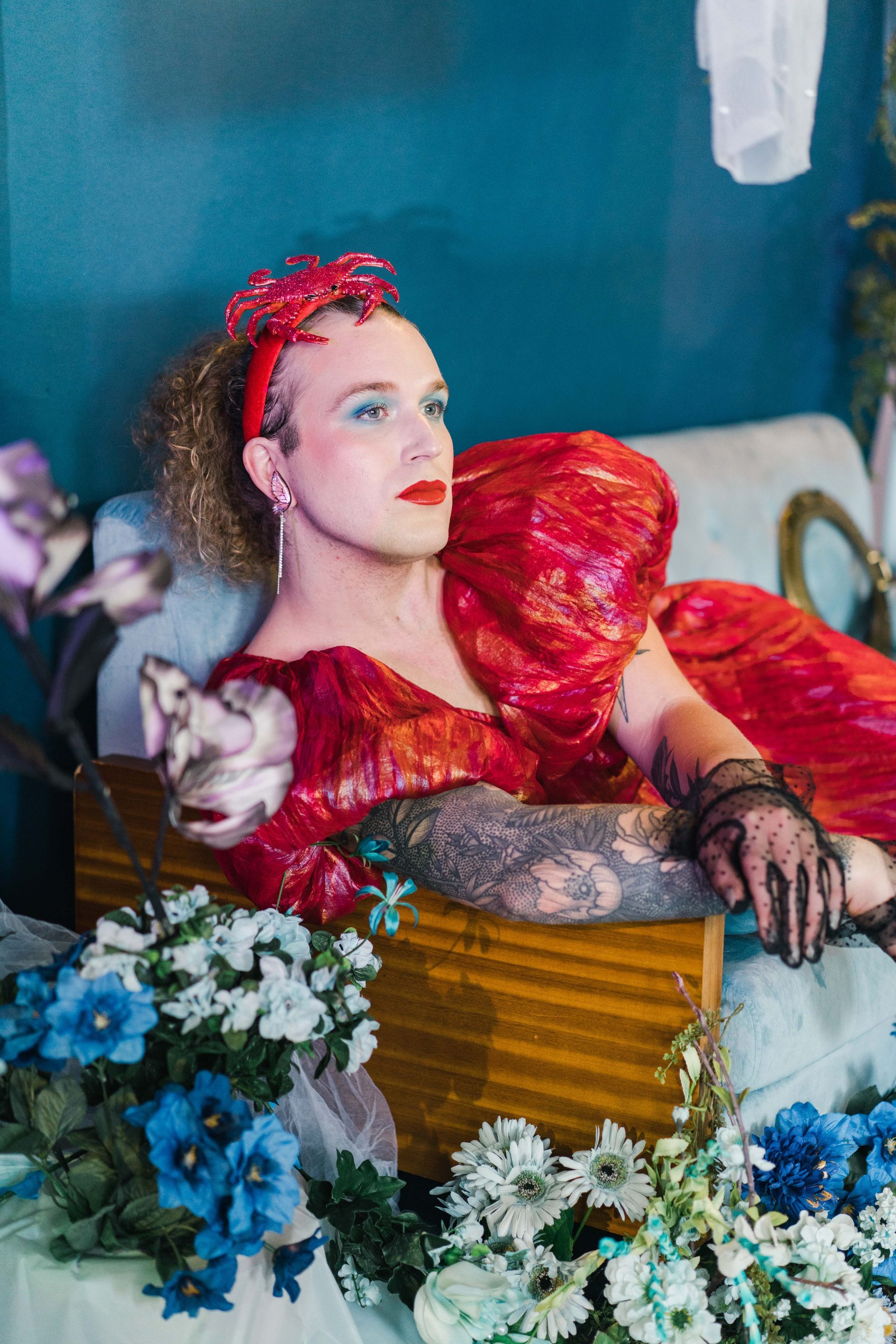 A woman in a red dress is laying in a box surrounded by flowers for a photo shoot.