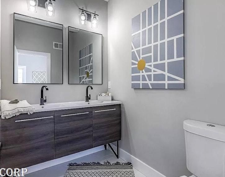 Modern bathroom with double vanity, two mirrors, gray walls, and abstract wall art.