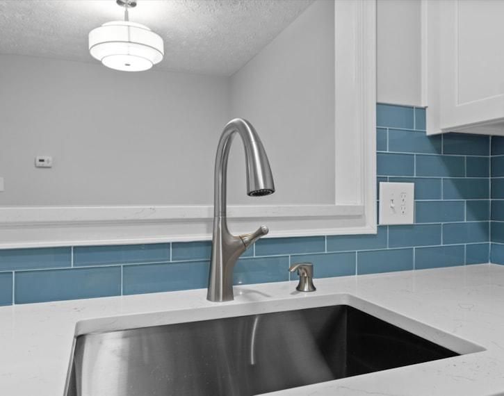 Modern kitchen sink with stainless faucet, white countertop, and blue tile backsplash