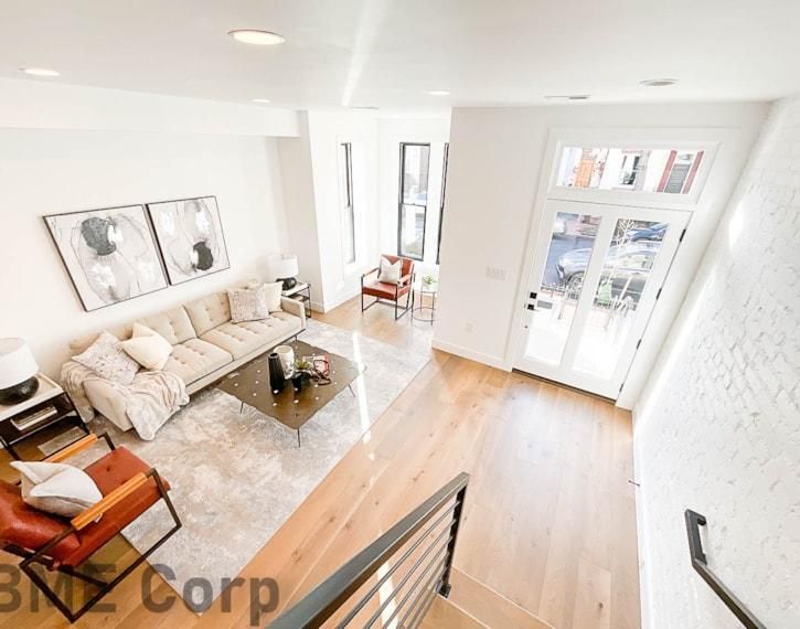 Bright modern living room with beige sofa, orange chair, wooden floor, and large windows.