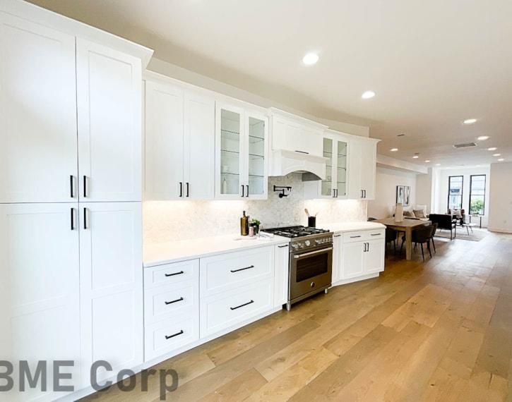 Bright modern kitchen with white cabinets, wood floor, black stove, and open dining area