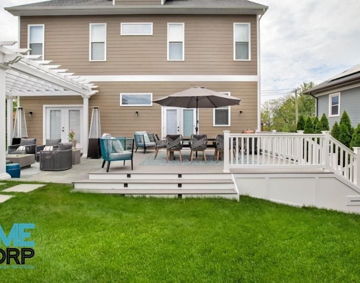 Backyard deck with patio furniture, umbrella, and white railing behind a green lawn