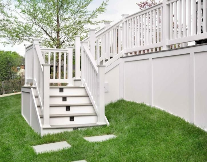 White outdoor staircase with railings leading up to a raised deck beside a grassy yard