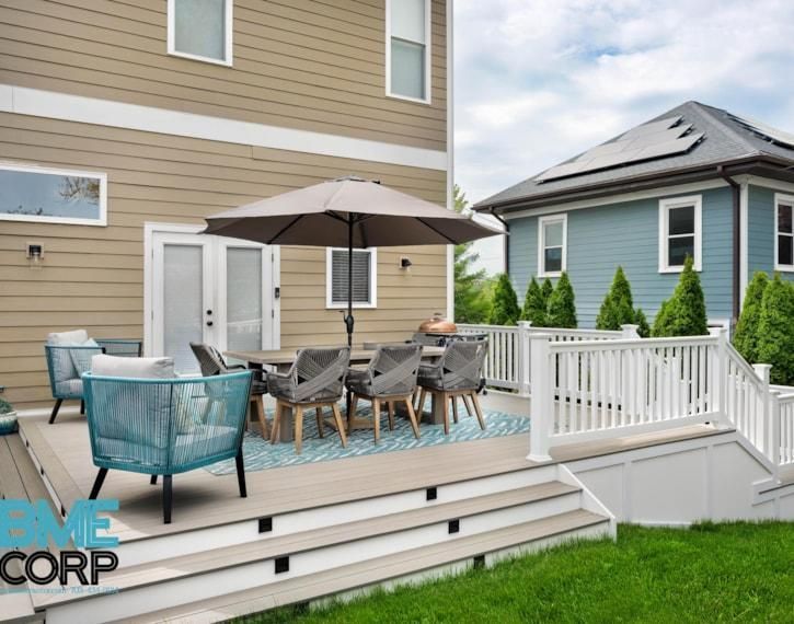 Patio deck with outdoor dining set, umbrella, and white railing beside a tan house in a suburban yard