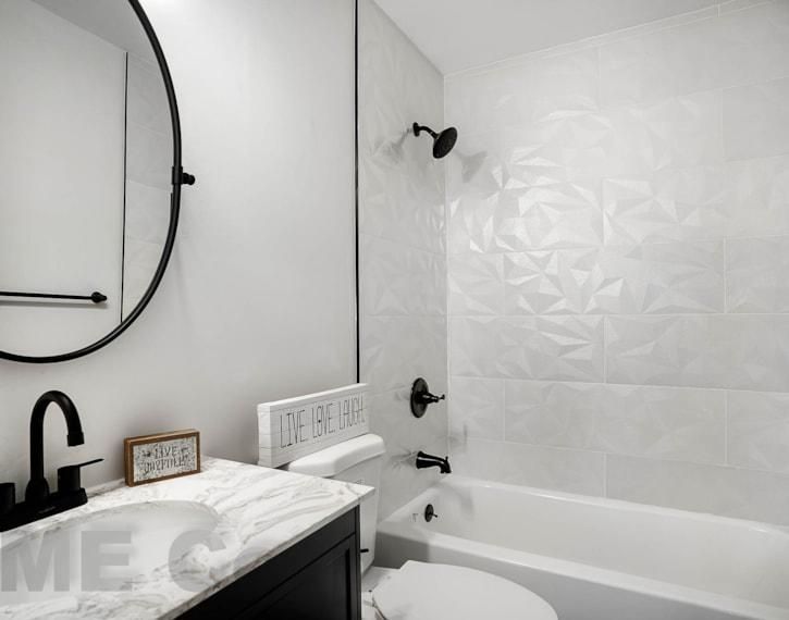 Modern black-and-white bathroom with round mirror, black faucet, and bathtub with white tile wall