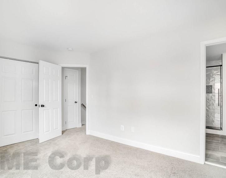 Bright empty bedroom with beige carpet, white walls, closet doors, and open door to hallway and bathroom.