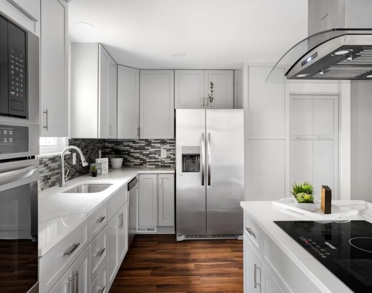 Bright modern white kitchen with stainless steel appliances, dark wood floors, and black tile backsplash