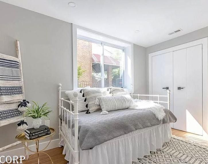 Bright bedroom with white bed, gray bedding, large window, and closet doors