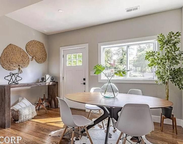 Bright dining room with oval table, white chairs, large window, and woven wall decor