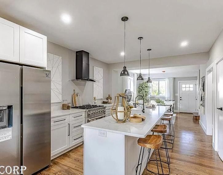 Bright modern kitchen with stainless fridge, white island, wood floors, and pendant lights