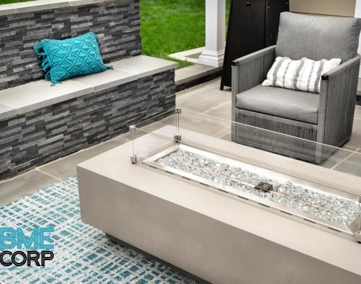 Modern patio lounge with gray stone seating, turquoise pillow, gray chair, and white fire table on tiled floor