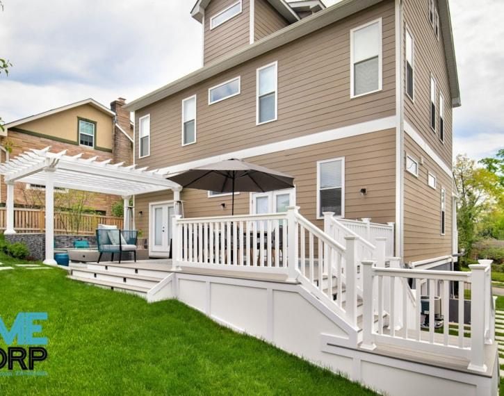 Backyard deck with white railings, pergola, and tan siding beside a two-story house