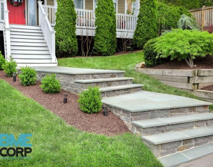 Backyard stone steps and landing beside a house, with a grassy slope and shrubs