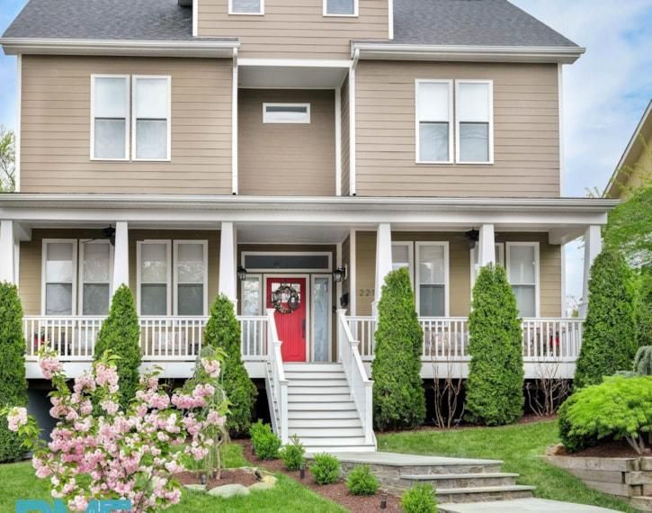 Two-story beige house with white porch, red front door, and landscaped front yard