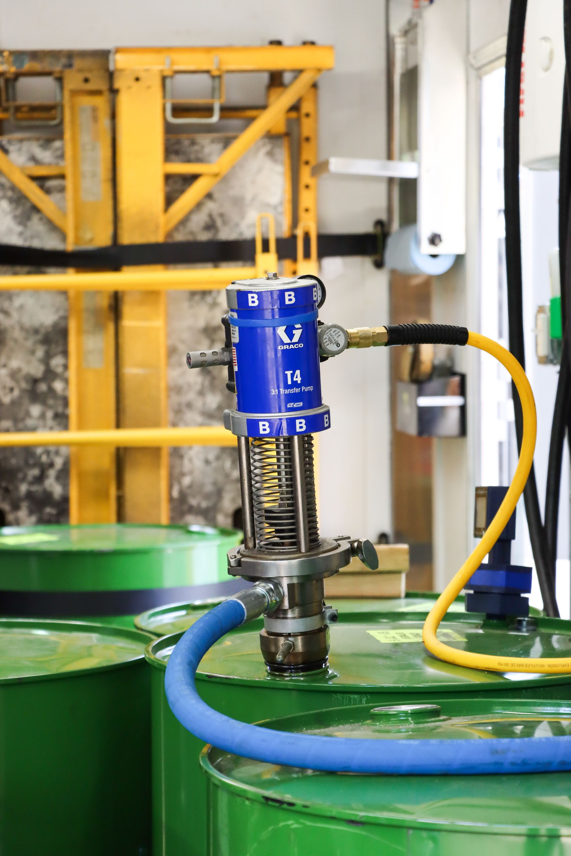 A blue pump with a yellow hose attached to it is in a room with green barrels.