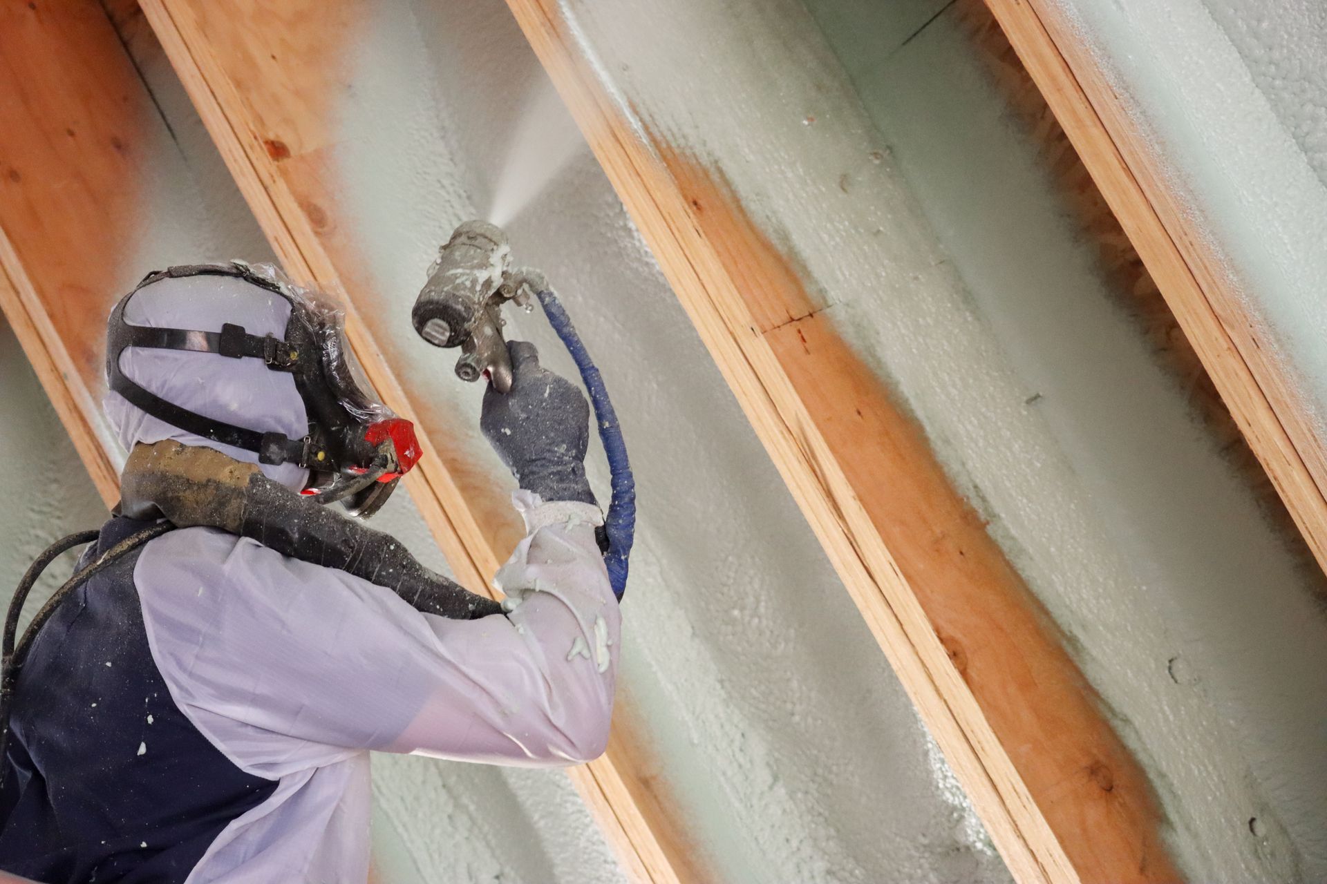 A man is spraying foam on the ceiling of a house.