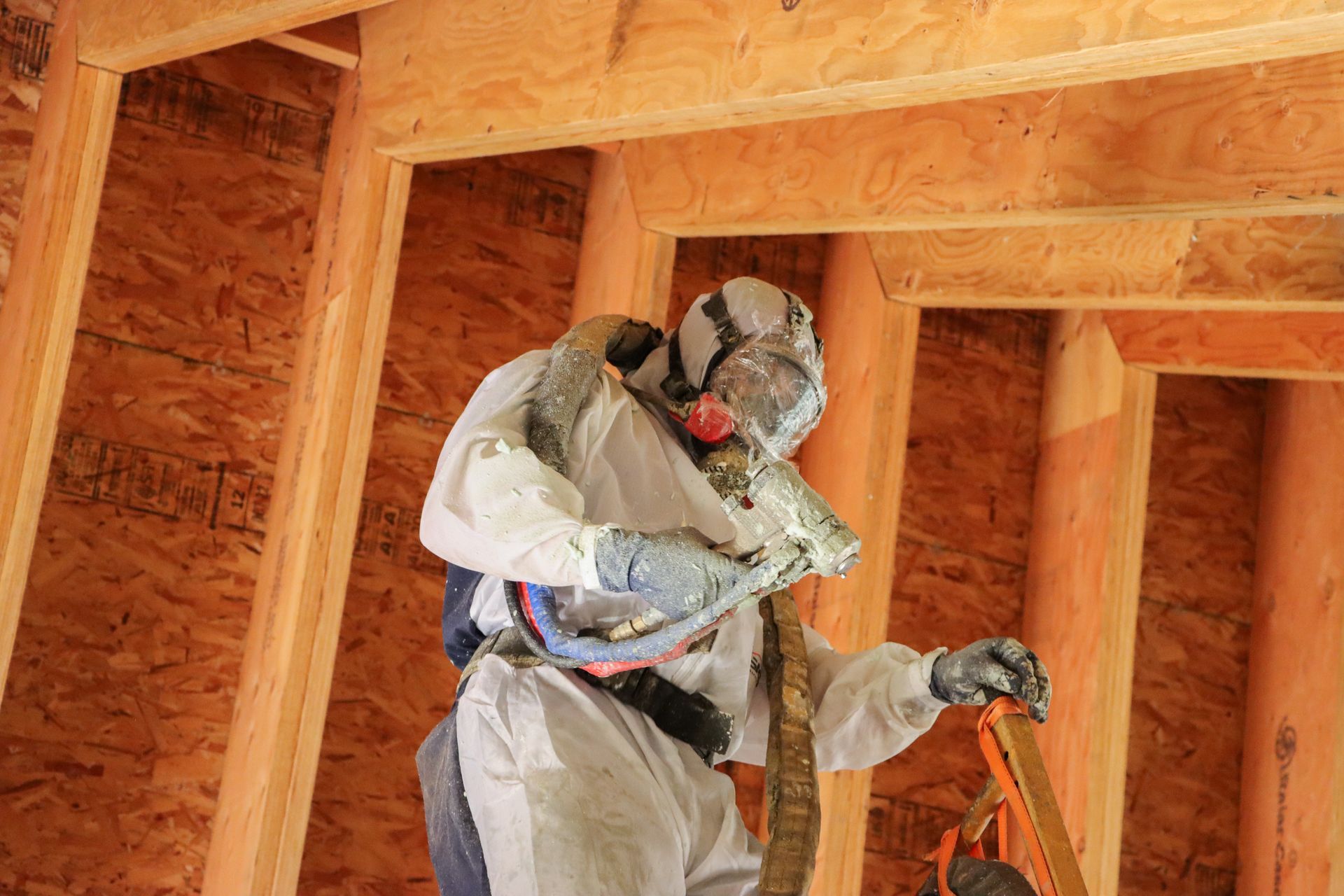 A man in a protective suit is spraying foam on a wooden structure.