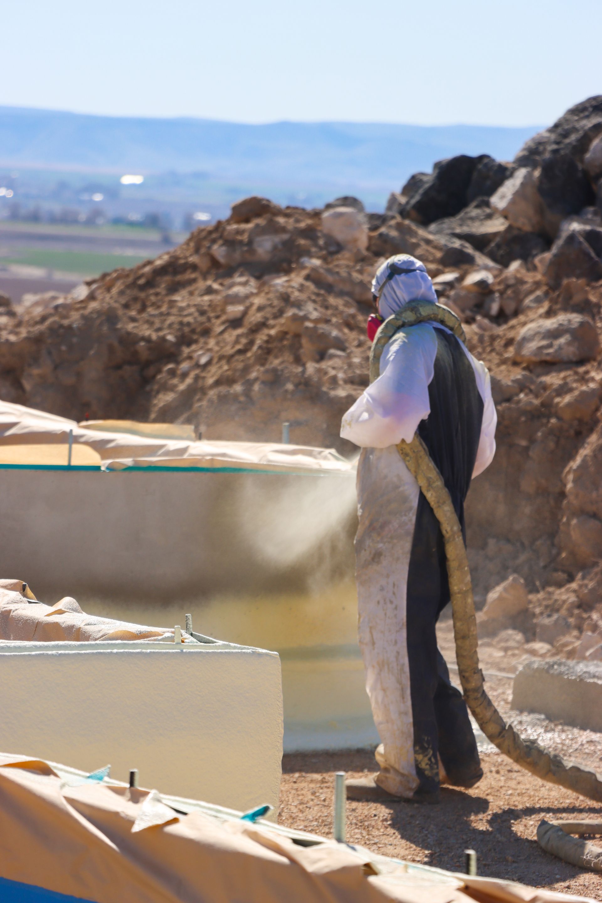 A man in a protective suit is spraying a wall with a hose.