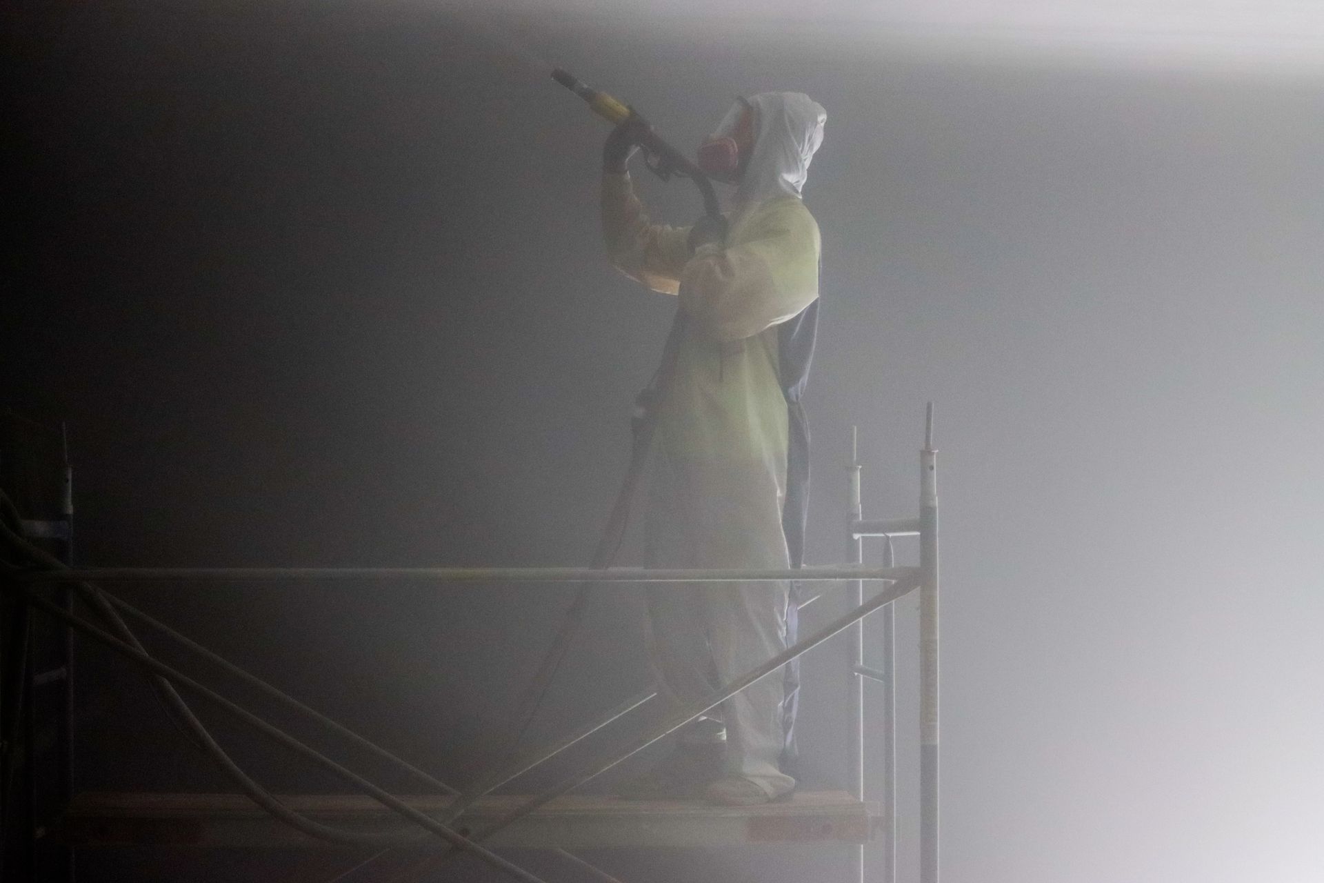 A man is spraying insulation on the floor of an attic.