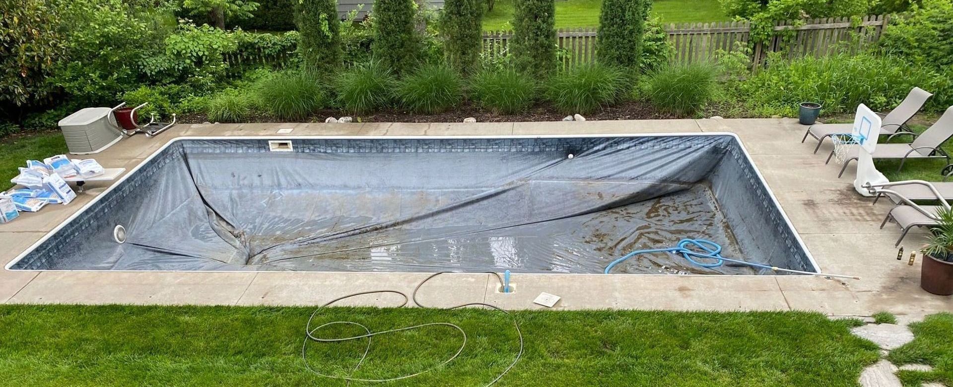 A rectangular pool covered with a tarp, surrounded by concrete and grass, with lounge chairs nearby.
