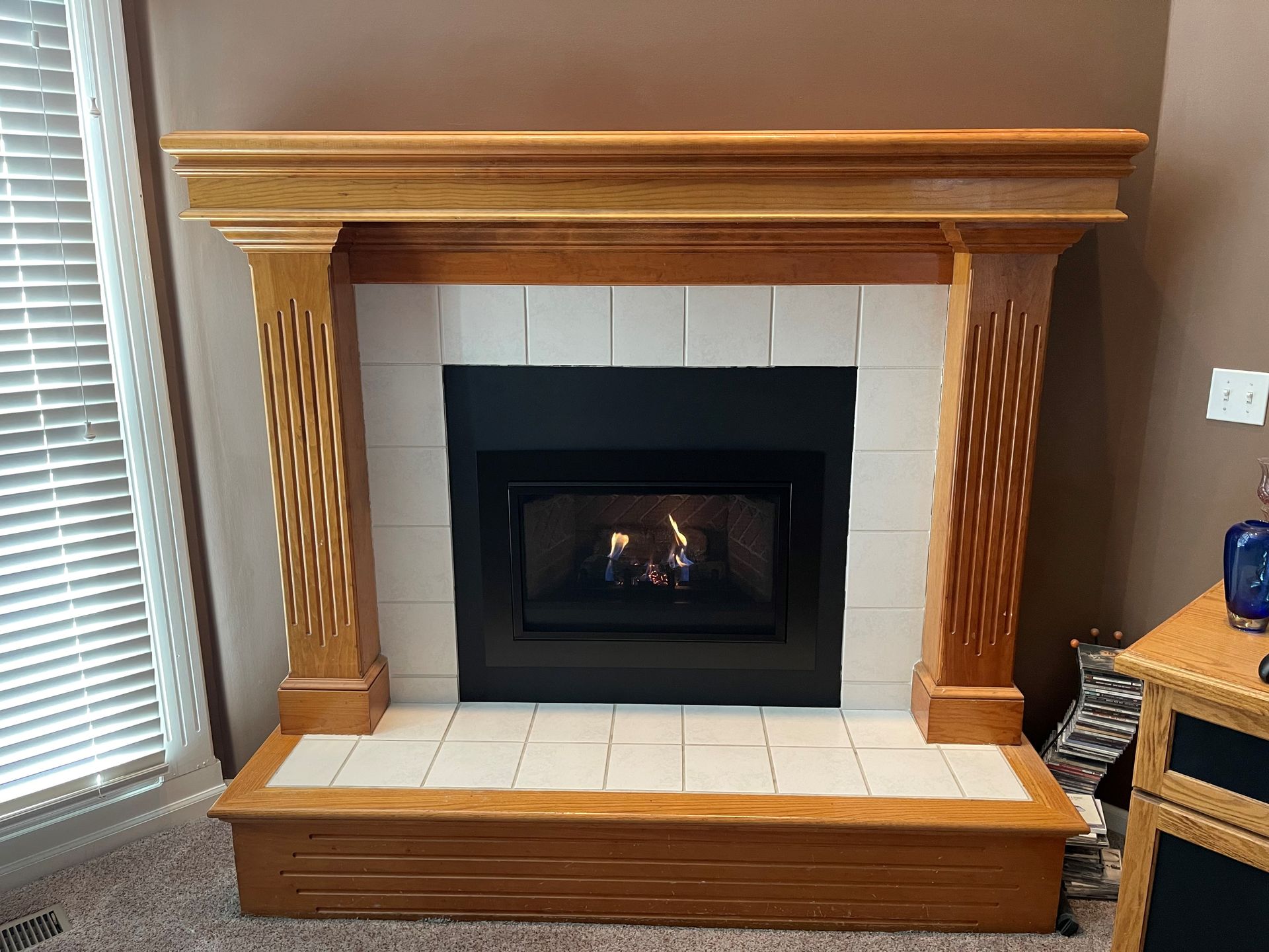Fireplace with wood mantel, white tile surround, and fire burning inside.