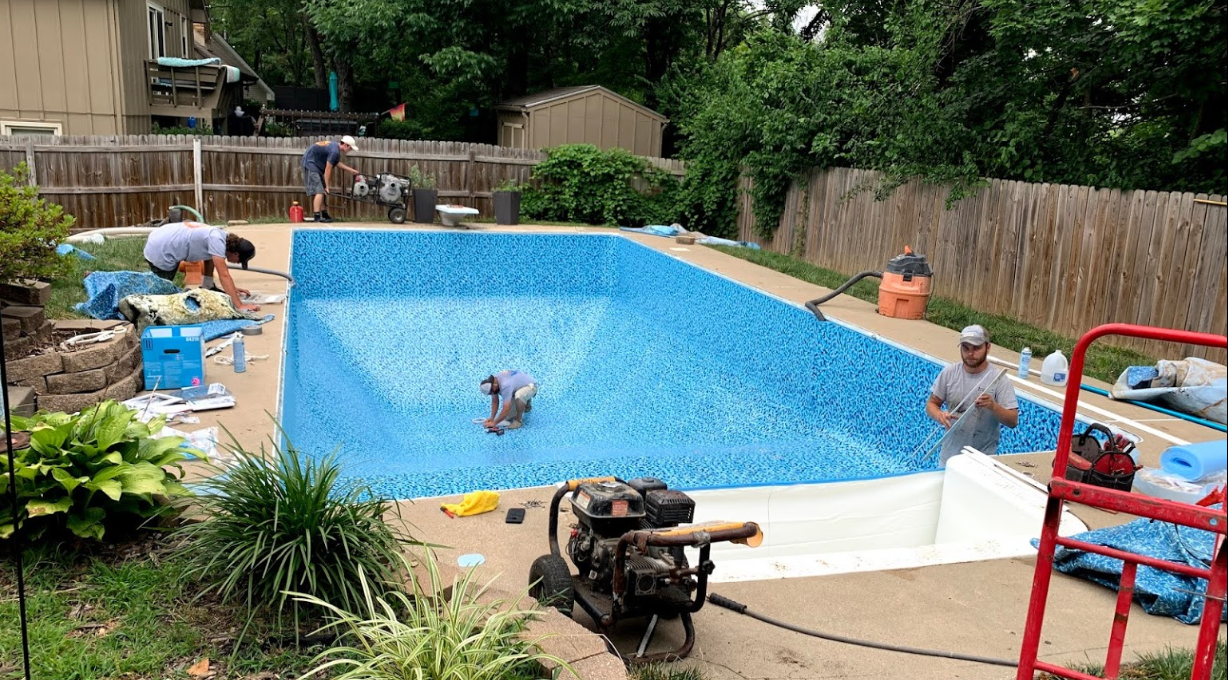 Workers installing a blue tiled pool liner in a backyard.