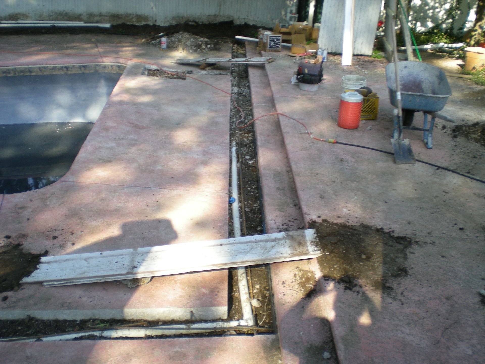 Poolside construction: concrete path with a trench, tools and materials.