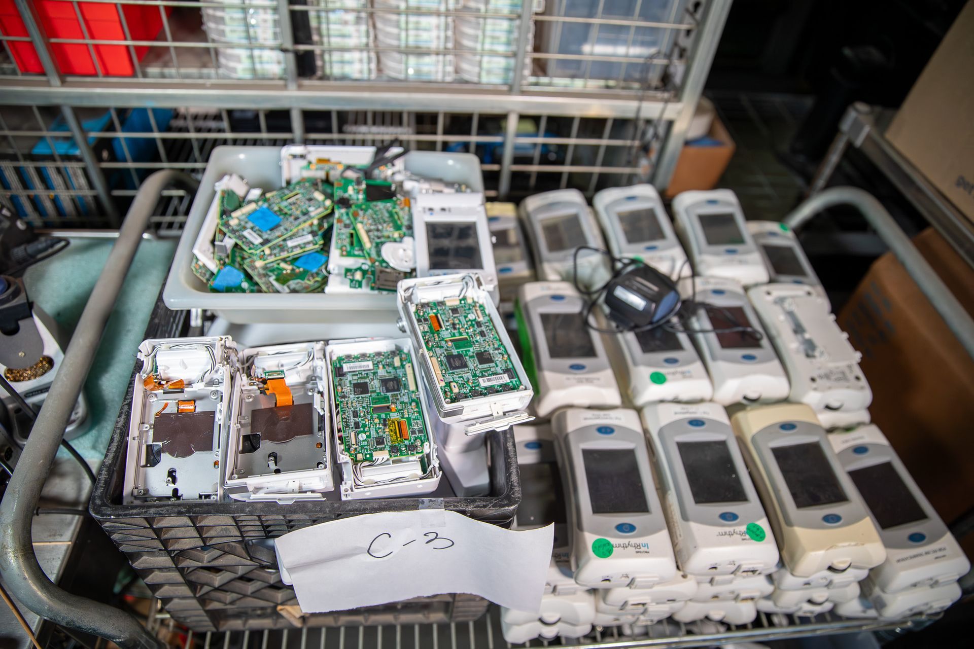 Green circuit board with electronic components, resting on a blue object, near a soldering iron and spools of solder.
