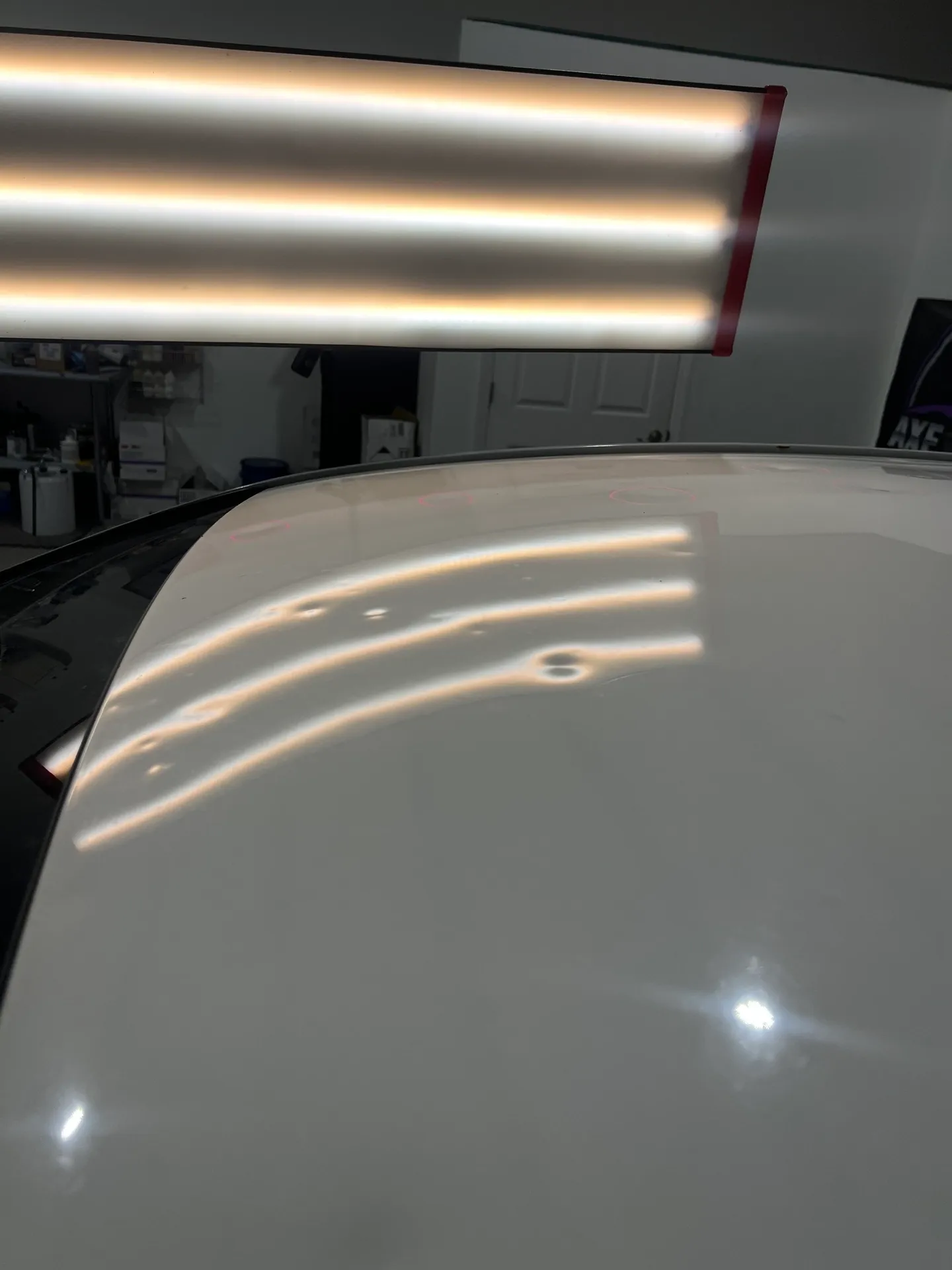 White car roof with several small dents under a fluorescent light.