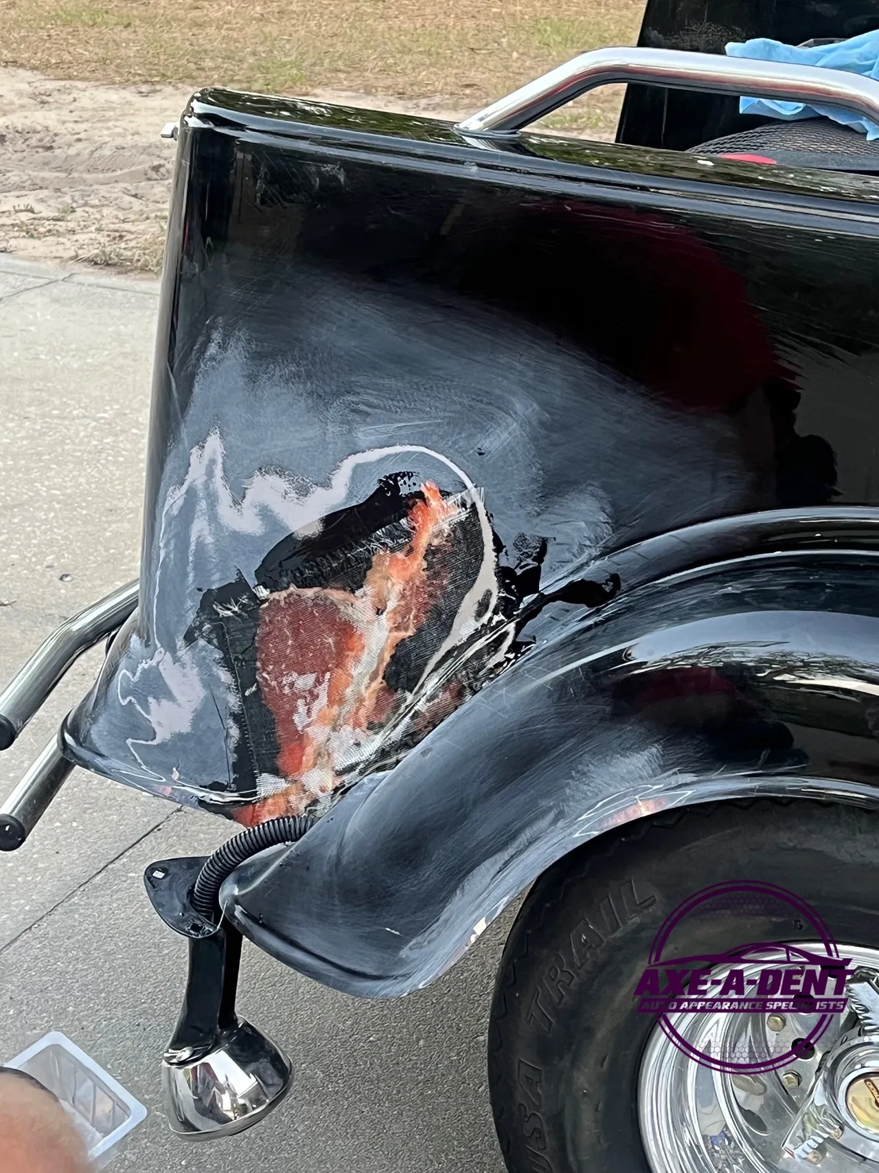 Black car rear with damaged body panel, showing primer and exposed metal.