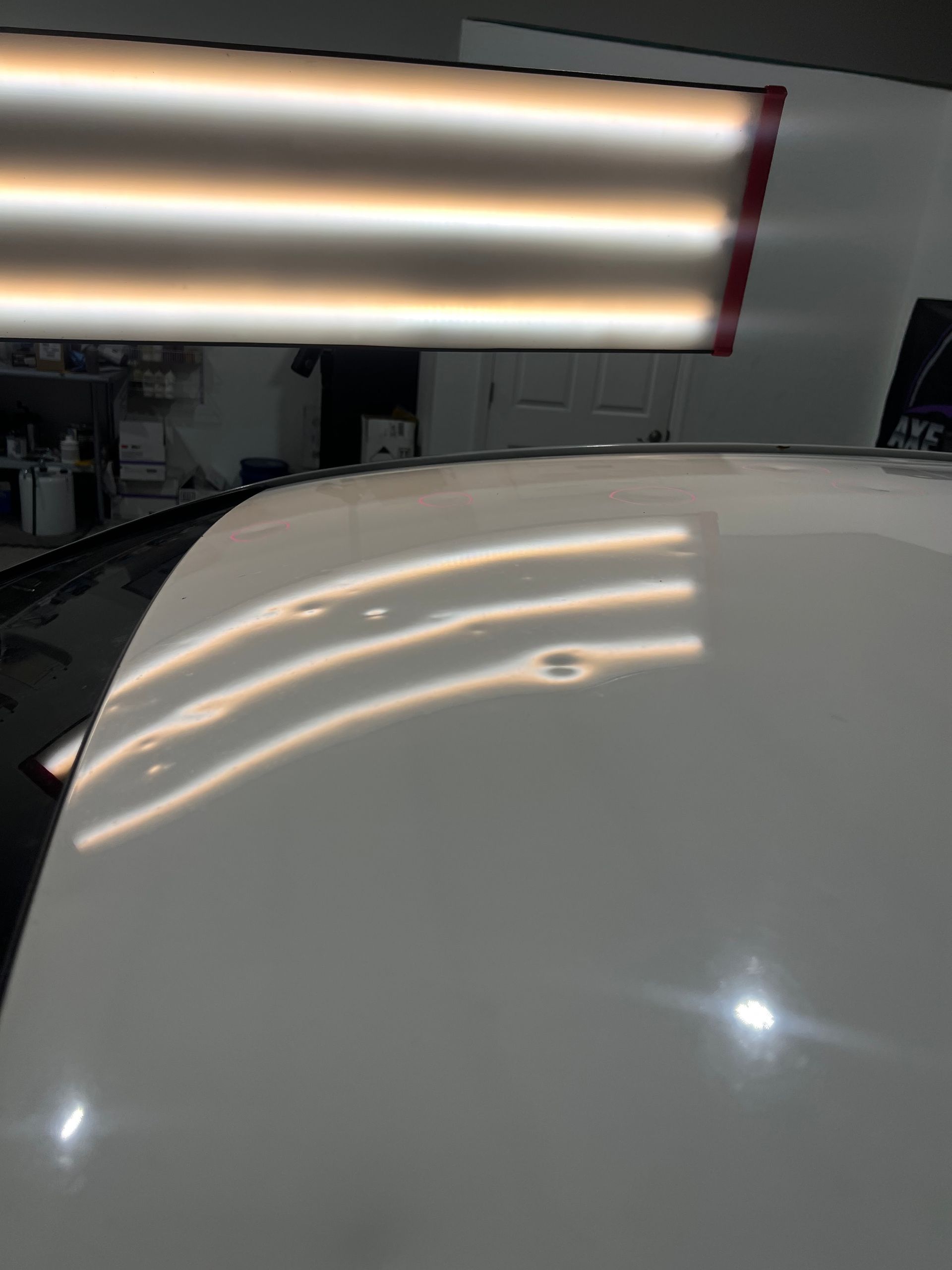 White car roof with several small dents under a light reflecting off the surface | Axe-A-Dent Auto Collision