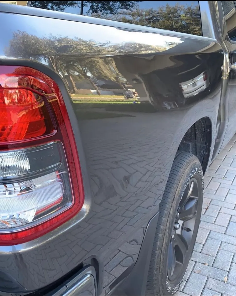 Dark gray pickup truck's rear side with taillight, tire, and body reflection.