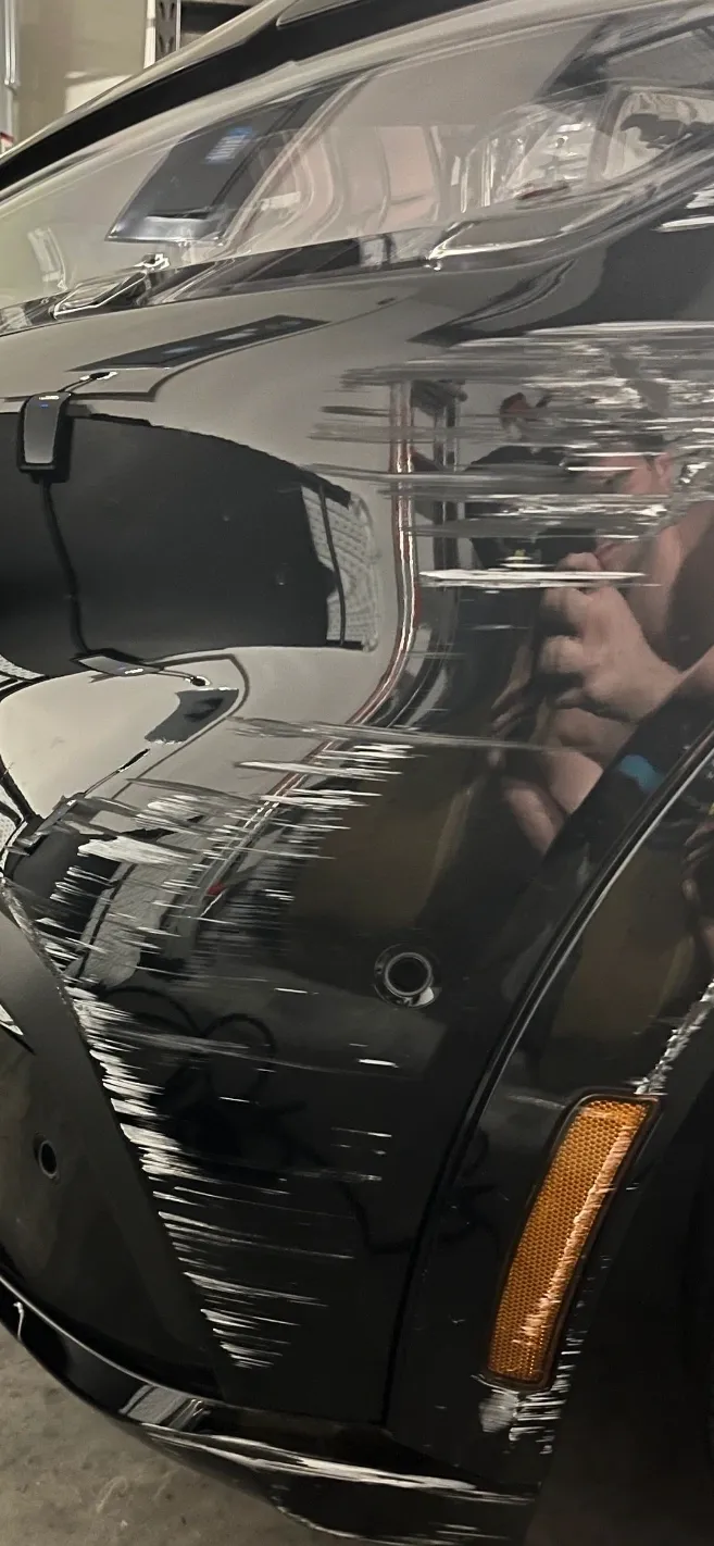 Damaged black car bumper with scratches and an amber side marker light.