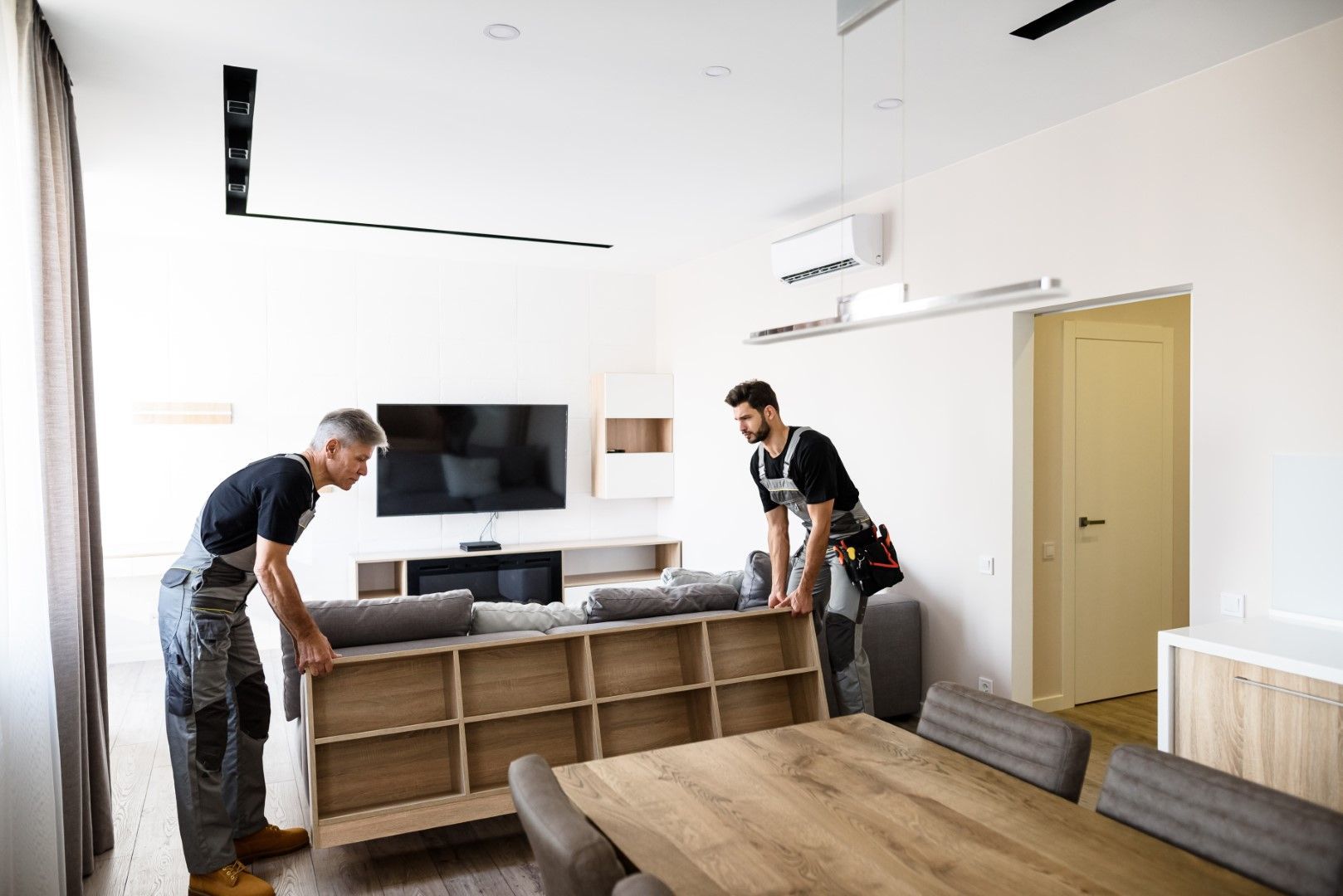 Two men are moving a couch in a living room.