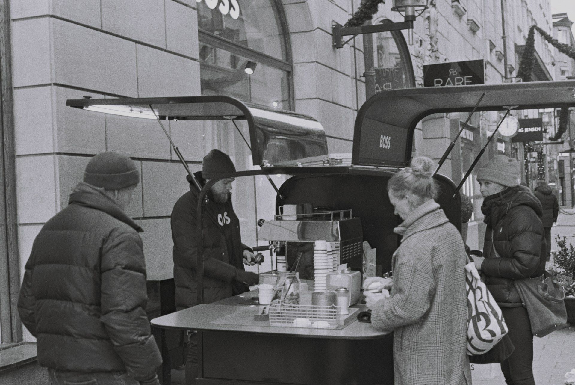 People gathered around a street food cart outside a building, with one person serving drinks or food.