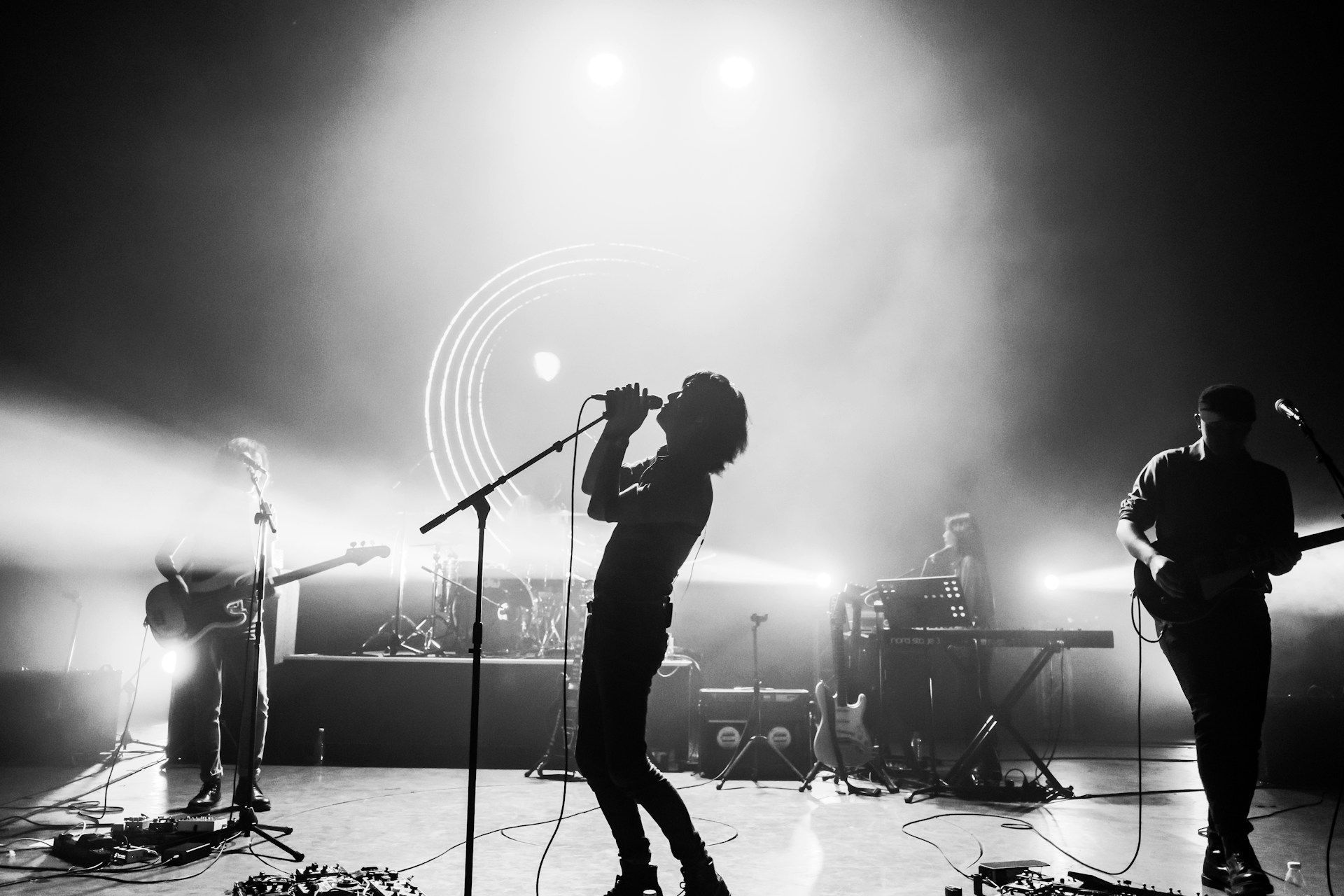 Silhouetted rock band performing on a brightly lit stage with microphones and guitars