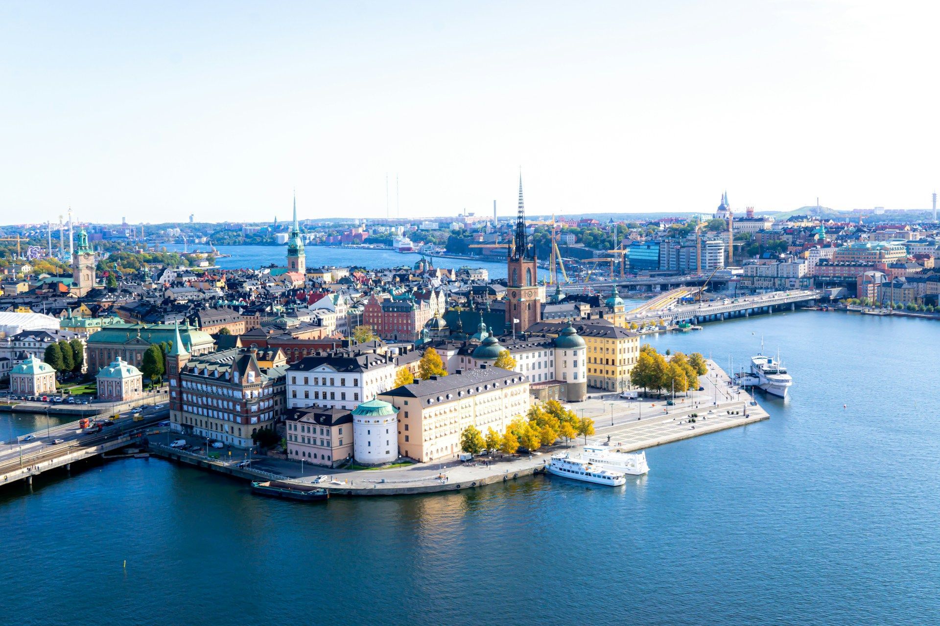 Aerial view of a coastal city with colorful waterfront buildings, church spires, and calm blue water.