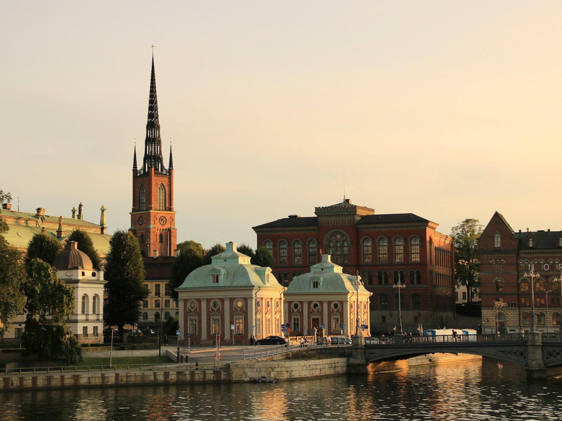 A view of Stockholm's Riddarholmen Church and historic buildings by the water at sunset.