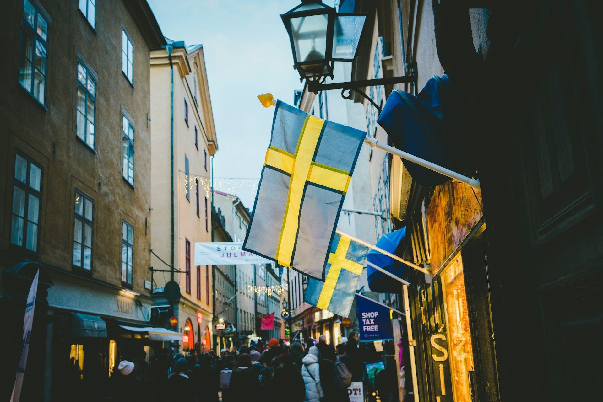 Crowded street with large Swedish flags hanging between buildings in Gamla Stan
