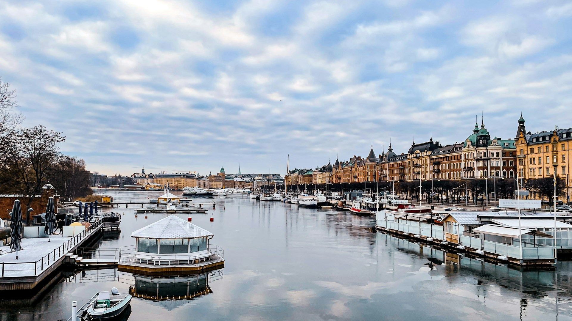 Snowy canal with boats and historic buildings under a cloudy winter sky