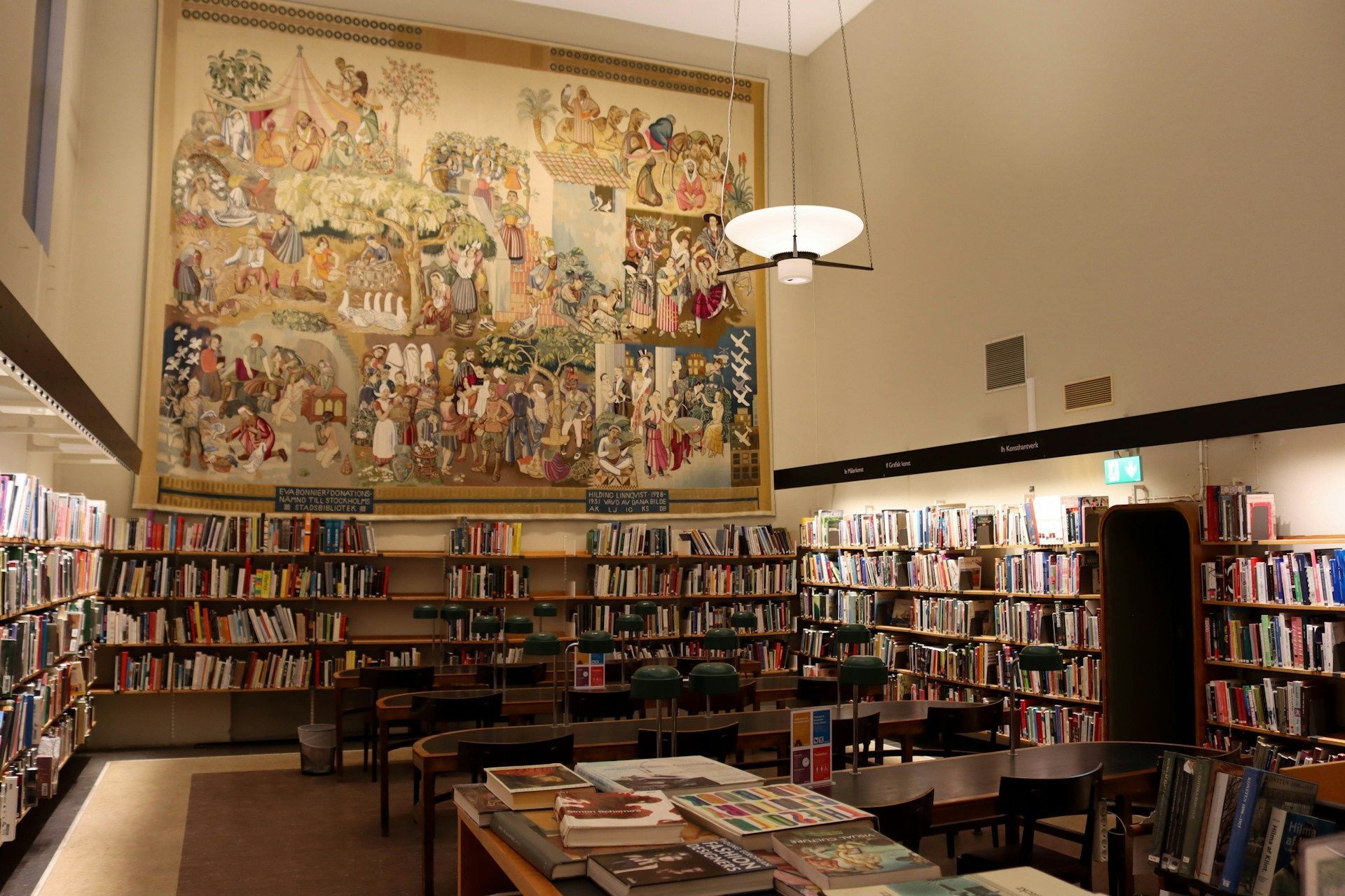 Library interior with bookshelves, tables, and a large, colorful mural on the wall