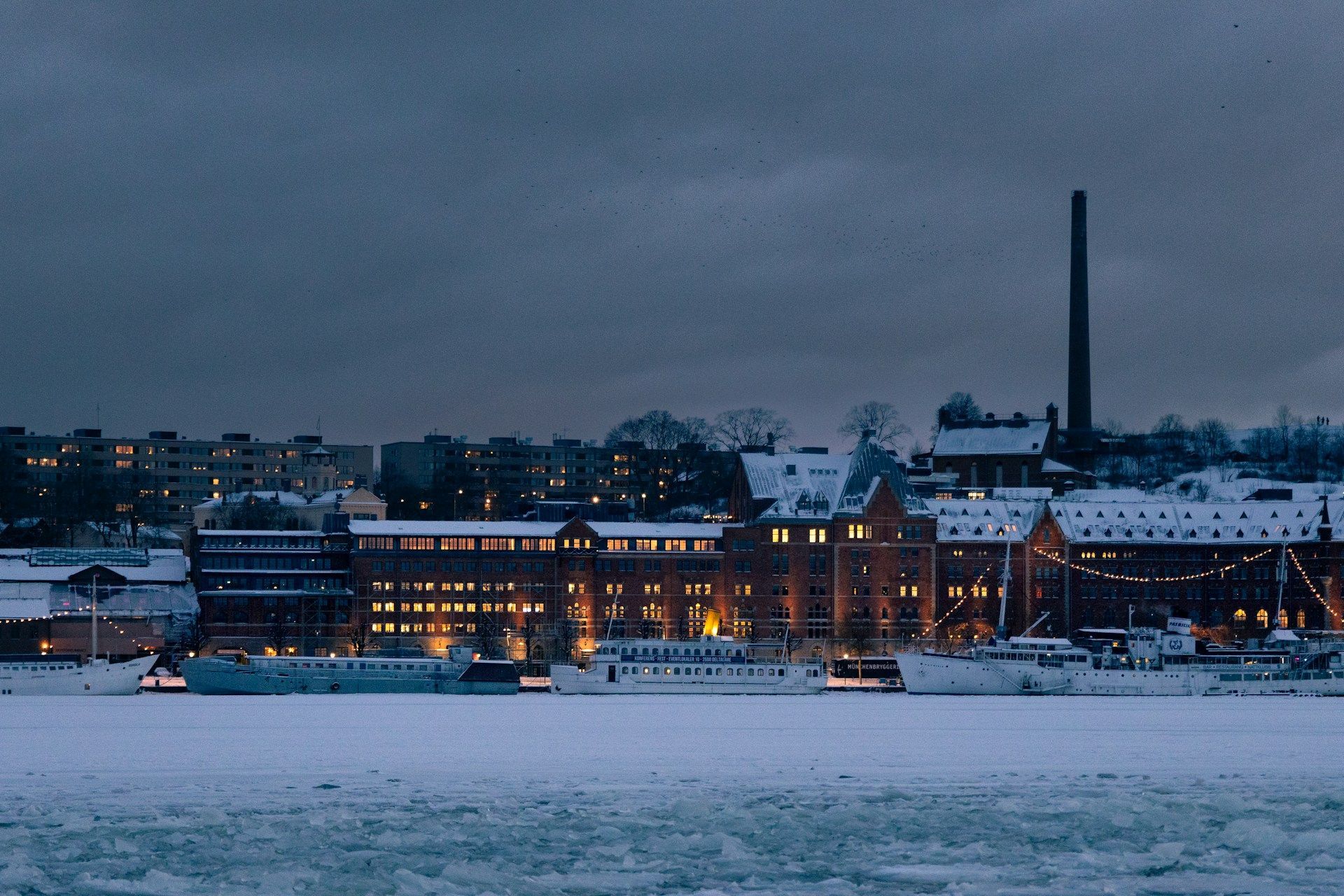 Snowy waterfront Stockholm buildings at dusk with warm lights reflecting on the frozen water