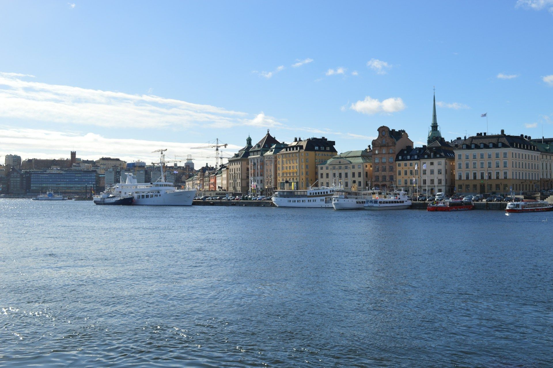 Stockholm waterfront with boats on calm blue water and historic buildings under a partly cloudy sky