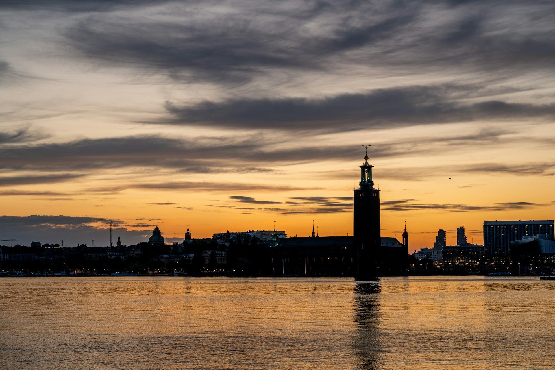 Silhouette of the Stockholm City Hall tower at sunset, reflected in the calm waters of Lake Mälaren.