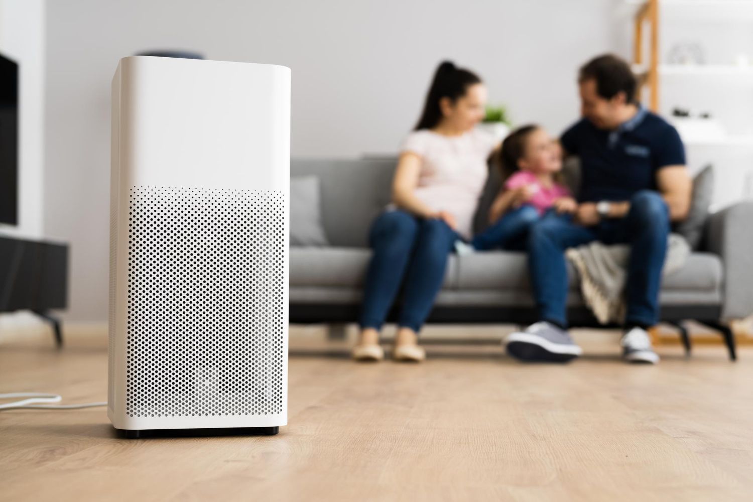 White air purifier in a living room with a blurred family on a couch in the background