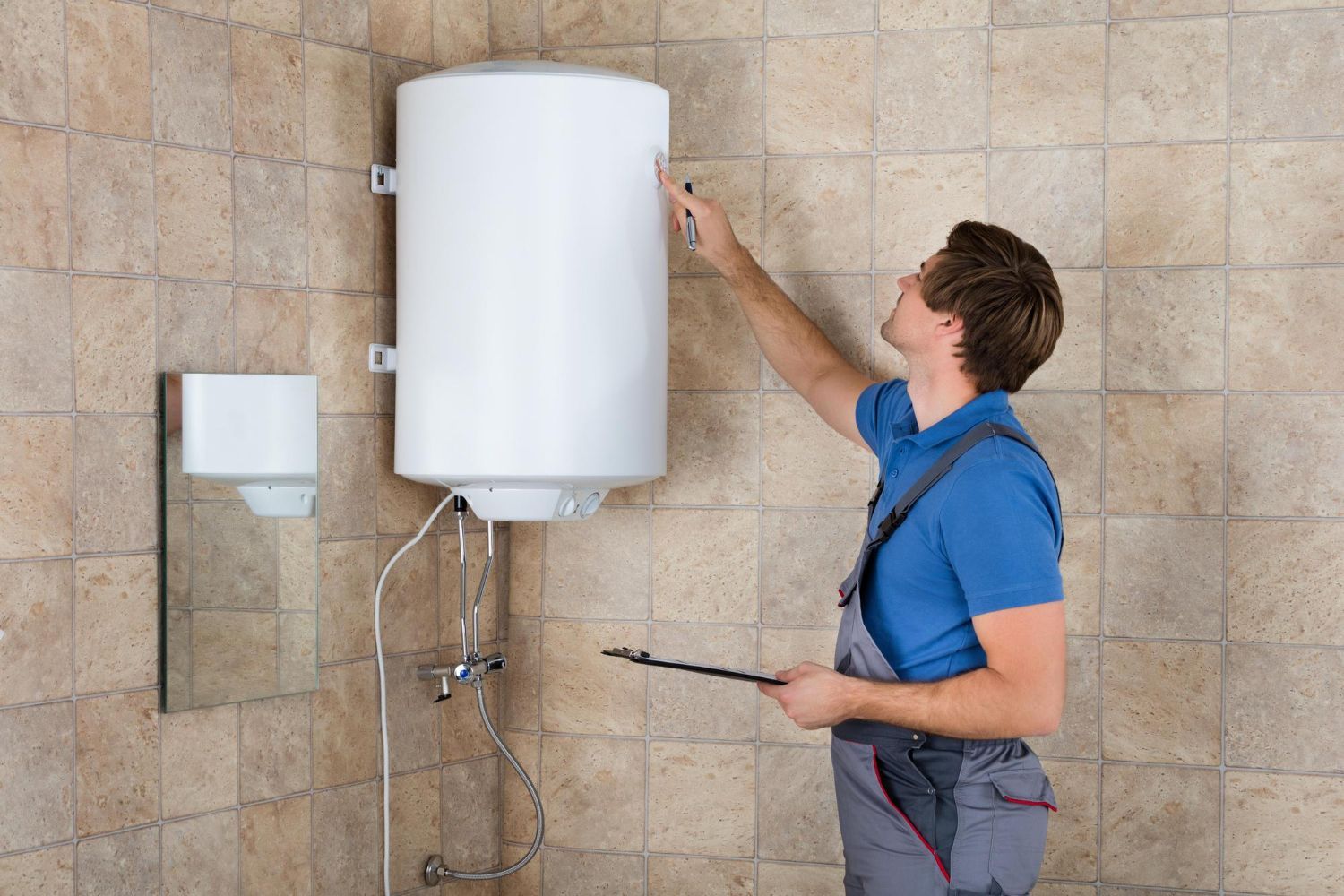 Technician inspecting a wall-mounted water heater with a screwdriver in a tiled room