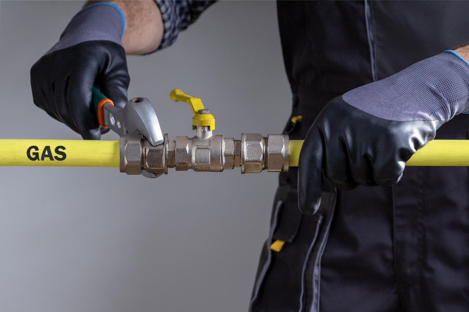 Gloved hands tightening a yellow gas pipe valve with a wrench and pliers