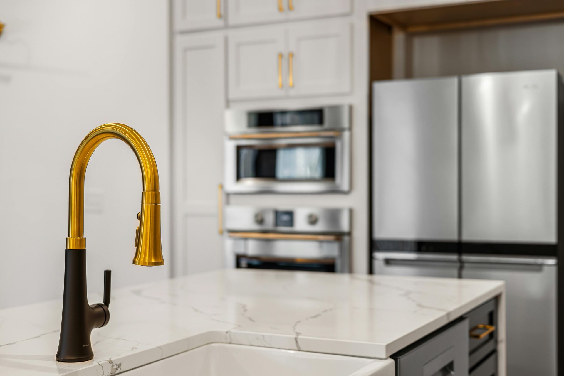 Modern kitchen with gold faucet, white island, stainless steel fridge, and built-in oven.