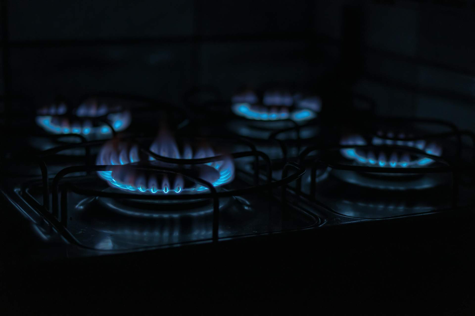 Blue flames on a gas stovetop in a dark kitchen